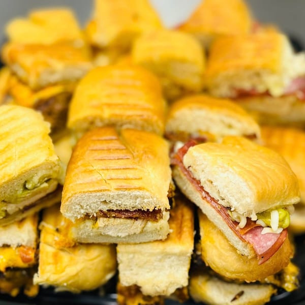 A close-up of a platter filled with various mini panini sandwiches, some with salami and pickles.