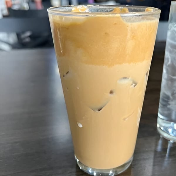 A tall glass of iced coffee with a thick layer of foam on top, next to a water glass.