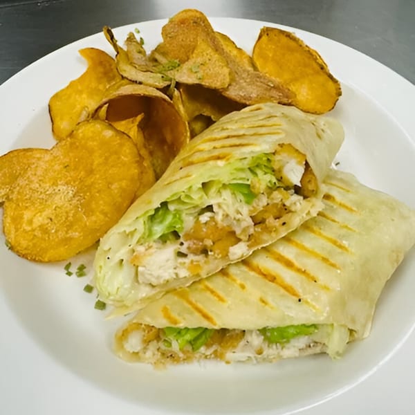 A grilled chicken wrap with lettuce and crispy chips on a white plate at Sims Cafe.