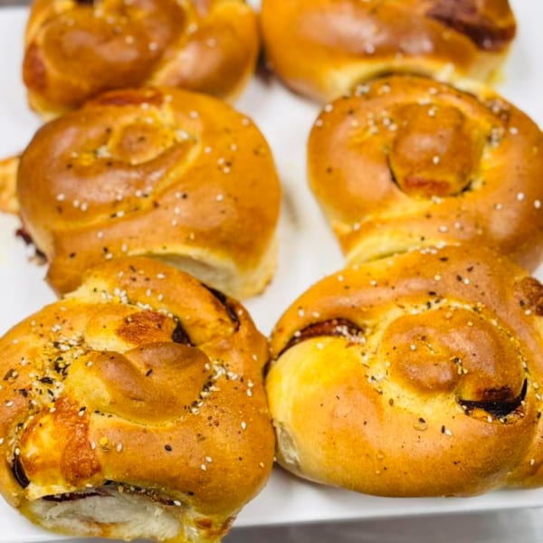 Golden brown braided pastries, sprinkled with sesame seeds and salt, on a white tray at Sims Cafe.