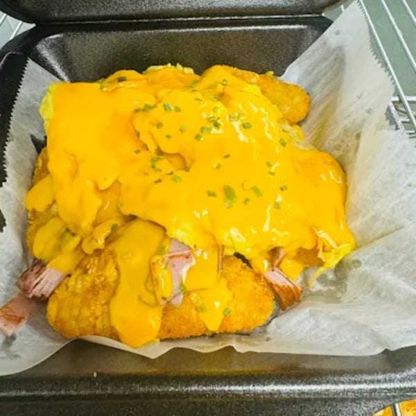A breakfast dish with hash browns, ham, scrambled eggs, and melted cheese, topped with chives.